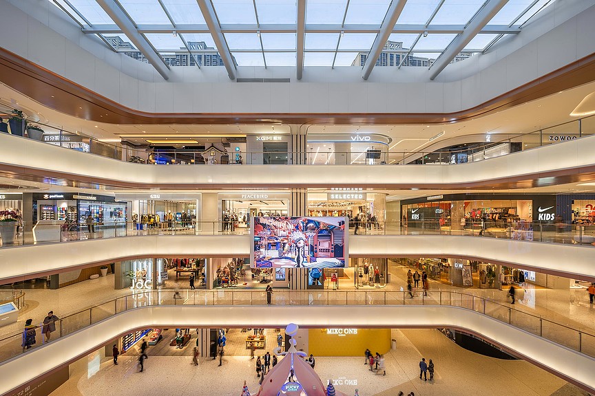 A large shopping mall with people and a large screen.